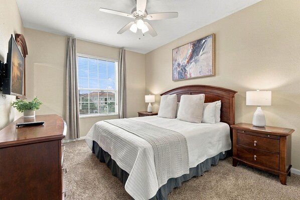 A hotel room with a bed, bedside tables, a desk, a ceiling fan, a window with curtains, and a painting on the wall. - 3BR Vista Cay, Conventions, Parks and Orlando Fun (Orlando)