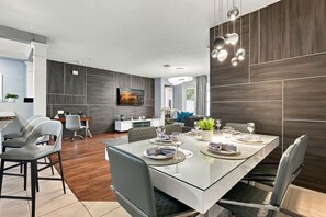 A modern dining area with a glass table, grey upholstered chairs, and a contemporary light fixture. - 3BR close to Convention Center and Theme Parks (Orlando)