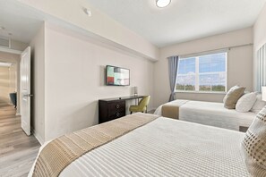 A hotel room with two beds, a desk, a chair, a TV, and a window with curtains. - Spacious 3BR condo, Perfect Orlando Home Base (Orlando)
