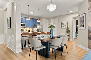 A modern kitchen with blue cabinets, a dining area with a wooden table and chairs, and a chandelier. - Luxury 3BR, Modern Design, Lake Views, Vista Cay (Orlando)