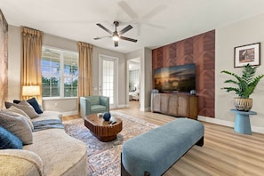 A living room with a sofa, armchair, coffee table, and a television on a wooden wall. - Luxury 3BR, Modern Design, Lake Views, Vista Cay (Orlando)