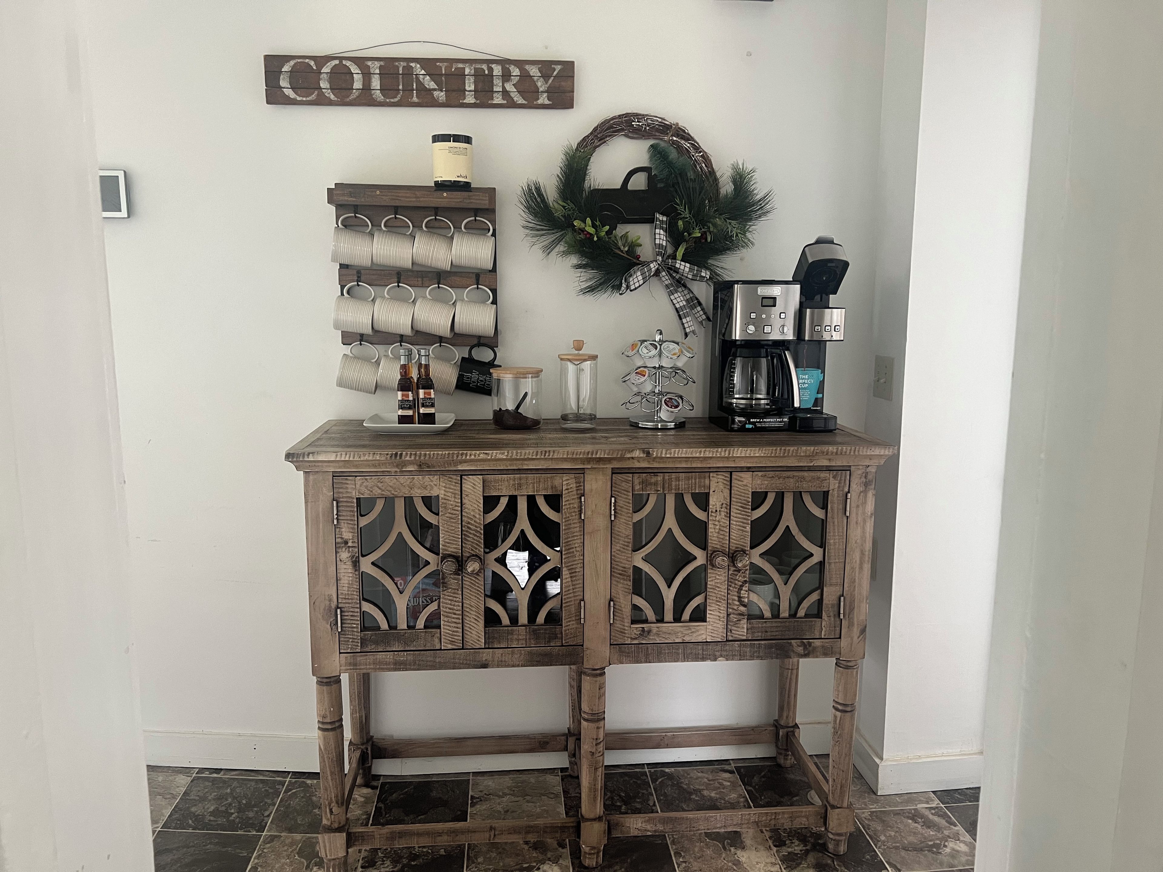 A wooden console table with a decorative metal tray, a coffee maker, and a wall-mounted sign.