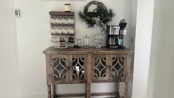 A wooden console table with a decorative metal tray, a coffee maker, and a wall-mounted sign.