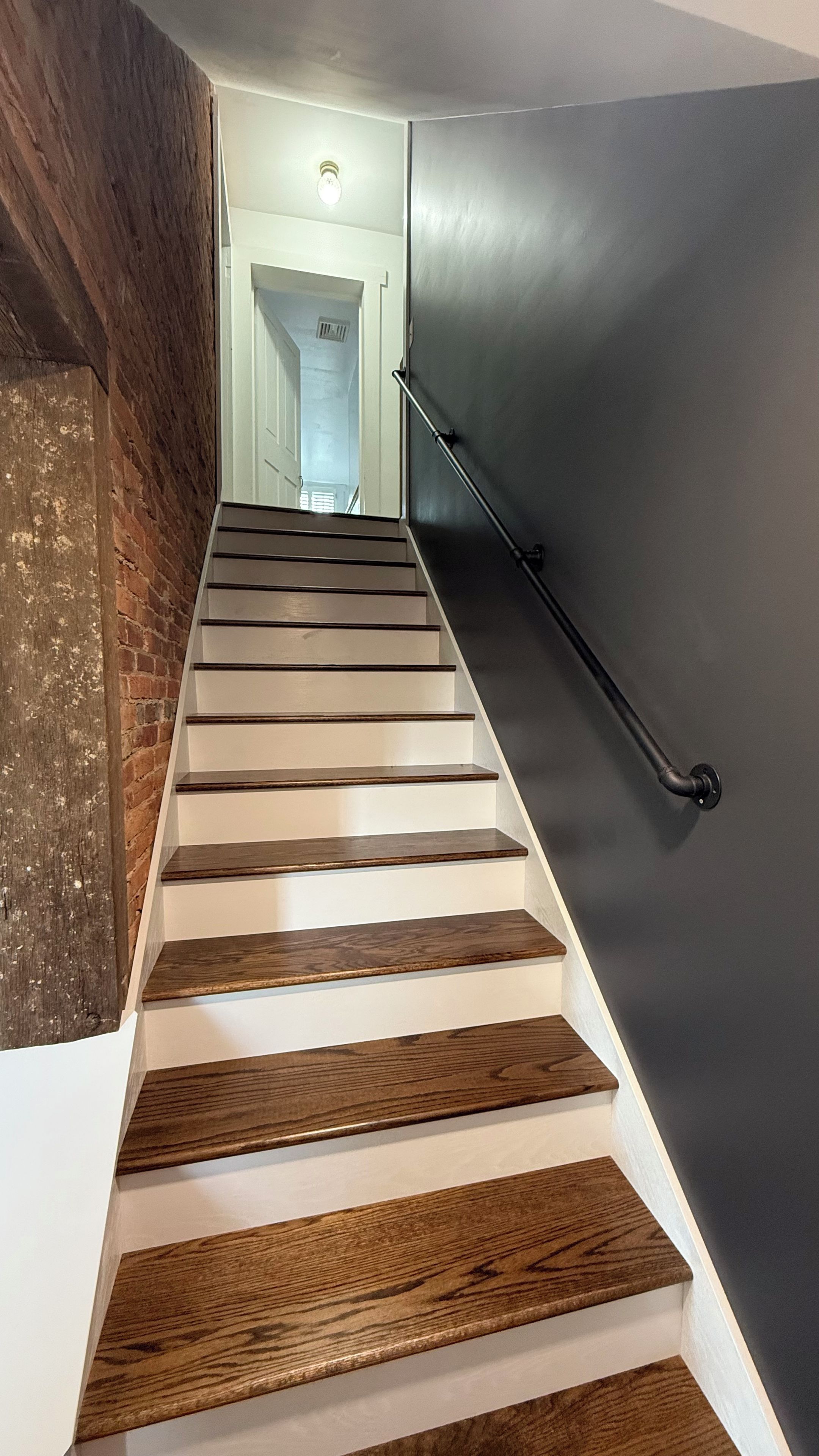 Eine Treppe mit Holzdielen und einer schwarzen Handlauf, die zu einem Raum mit einer weißen Tür und einer Leuchte führt.