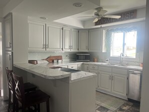 A kitchen with white cabinets, a marble countertop, a ceiling fan, and a sign that reads 'FARMHOUSE'.