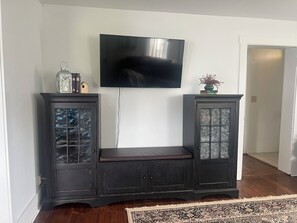 A living room with a dark wooden entertainment unit, a flat-screen TV mounted above it, and a patterned rug on the floor.