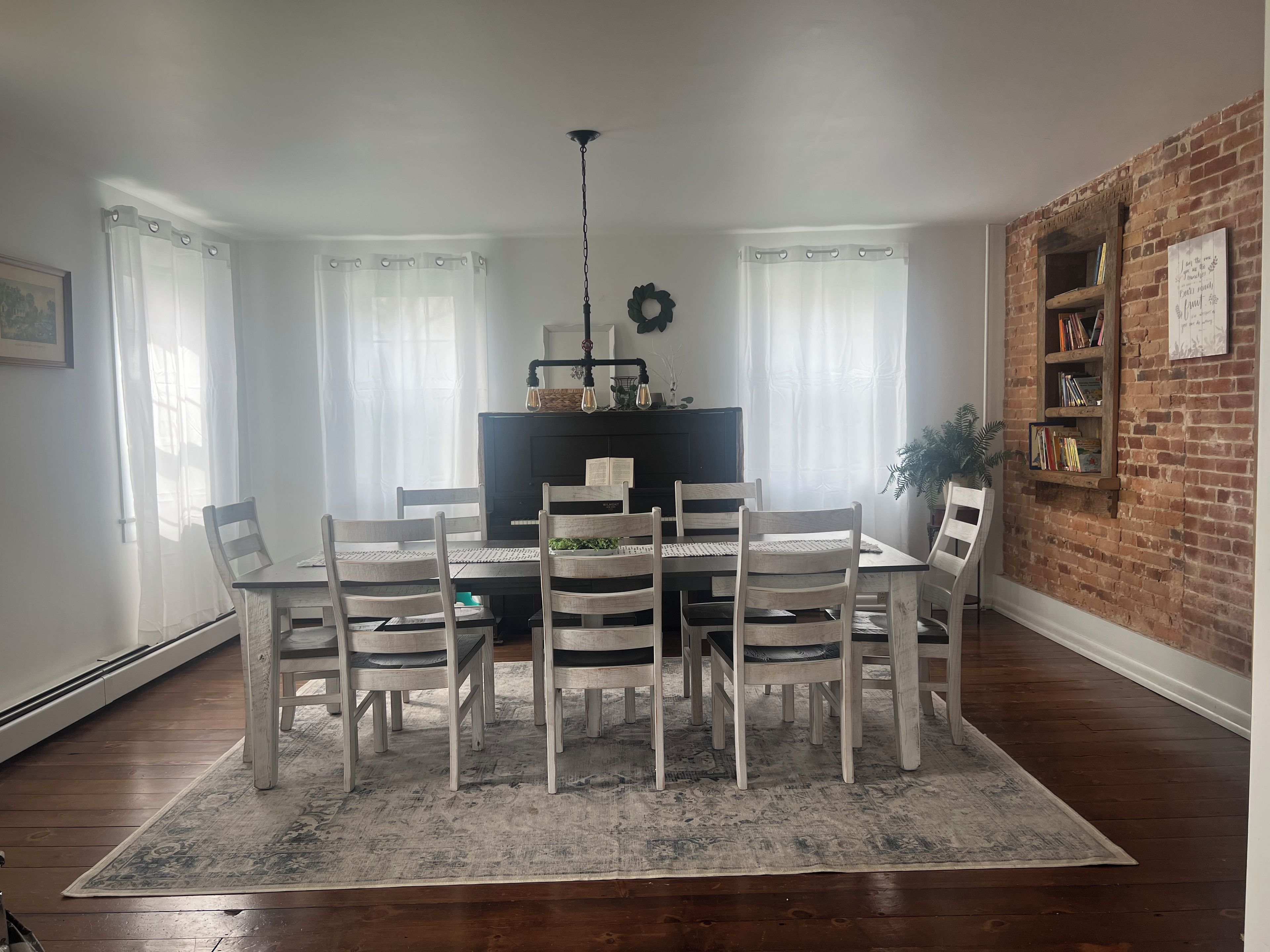A dining area with a table and chairs, a television, and a brick wall with a bookshelf.