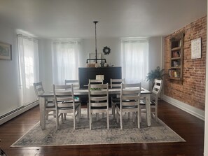 Un comedor con una mesa y sillas, un televisor y una pared de ladrillo con una estantería.