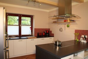 A modern kitchen with white cabinets, a black countertop, a window with blinds, and a red backsplash. - Cozy vacation home with a fireplace on a large garden lot, with a view of Lilienstein (Rathmannsdorf)