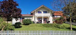 Een huis met twee verdiepingen, een balkon, een voortuin en een omheind erf.