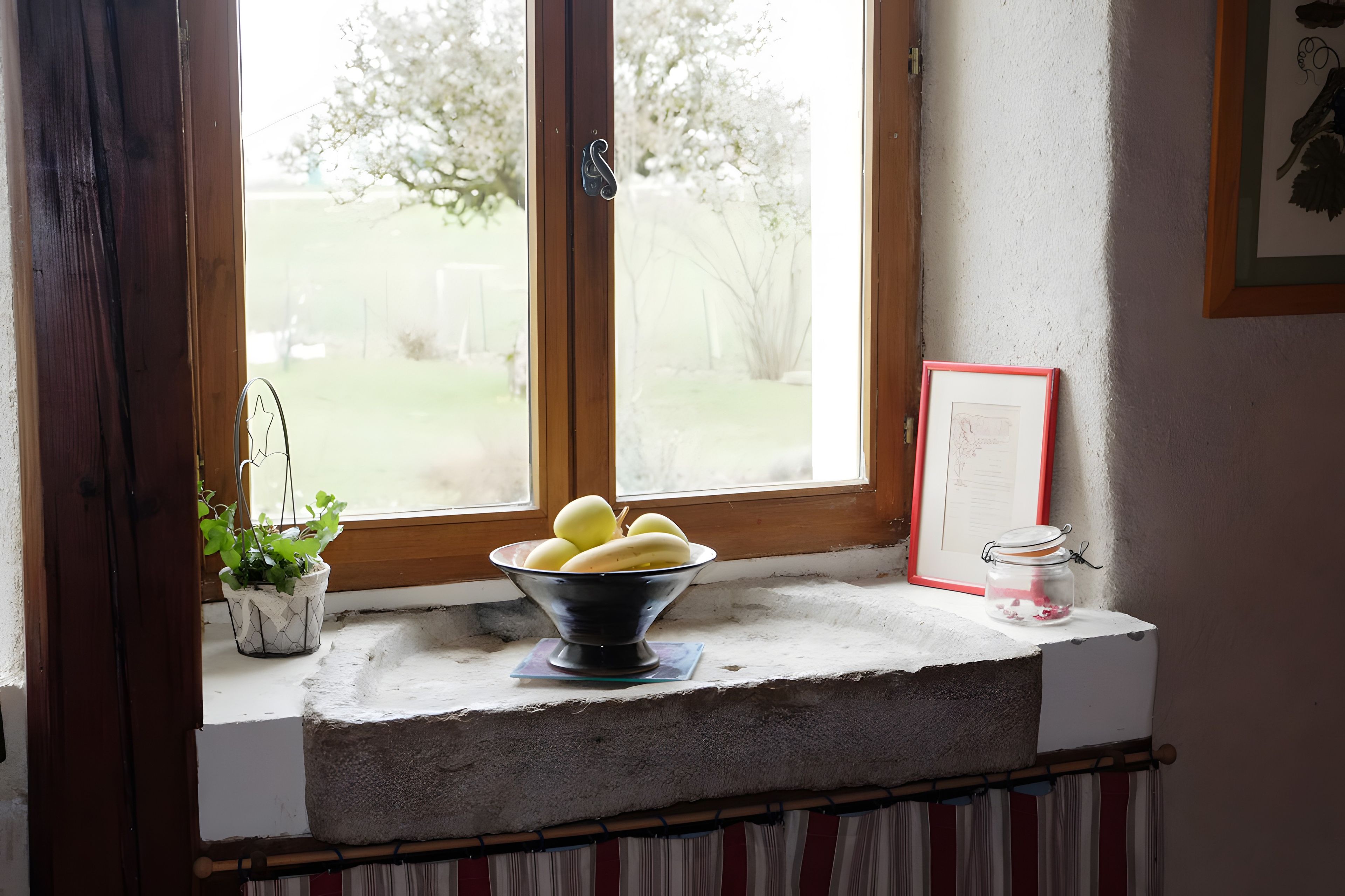 A window sill with a bowl of fruit, a potted plant, and a framed picture.