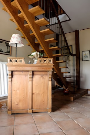 A wooden staircase with a railing, a cabinet with a lamp, and a vase with flowers.