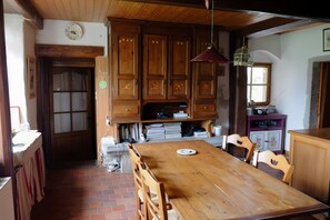 Ein Holzespeisetisch mit Stühlen, ein Küchenbereich mit Schränken, eine Uhr an der Wand und ein Fenster mit Blick.