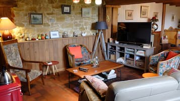 A cozy living room with a stone wall, wooden furniture, a television, and various decorative items.
