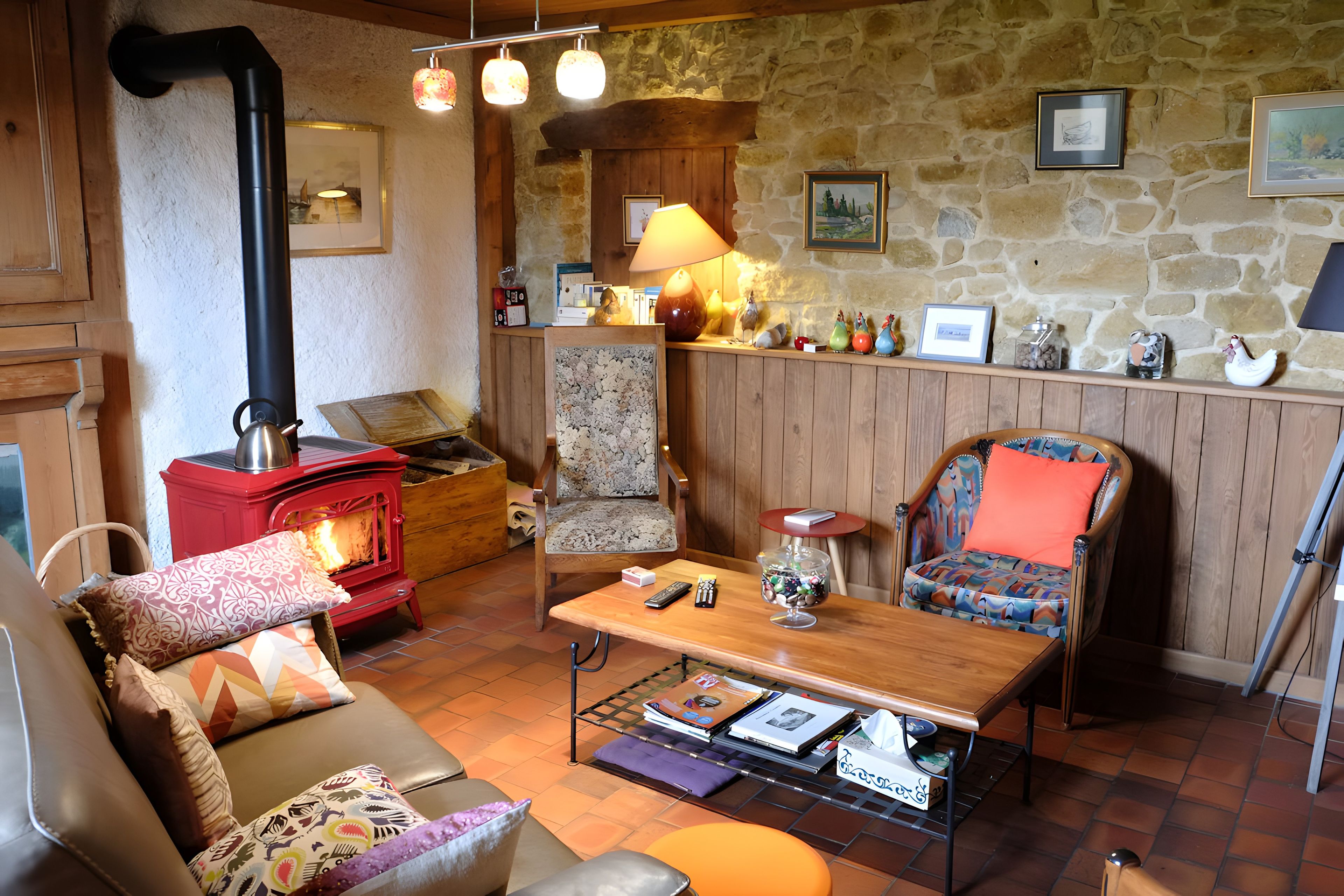 Un salon chaleureux avec une cheminée, un canapé en bois, un fauteuil, une table basse et un mur en pierre.