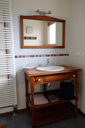 Ein Badezimmer mit einem Holzbadezimmerhocker, einem Spiegel, einem Waschbecken und einem Handtuchhalter.