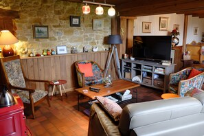 Ein gemütliches Wohnzimmer mit Steinwand, Holzmöbeln, einem Fernseher und unterschiedlichen Dekorationselementen.