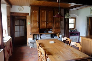 Ein Holzespeisetisch mit Stühlen, ein Küchenbereich mit Schränken, eine Uhr an der Wand und ein Fenster mit Blick.