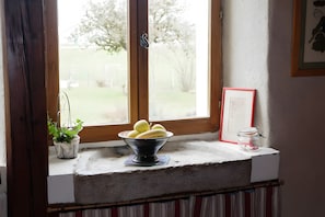 A window sill with a bowl of fruit, a potted plant, and a framed picture.