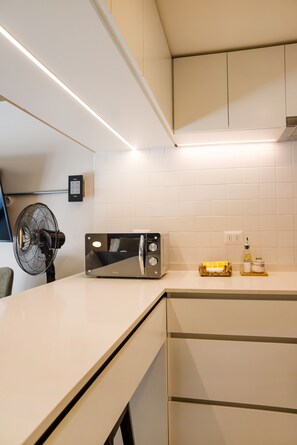 A modern kitchen with white cabinetry, a built-in microwave, and a toaster. There is a fan on the left and a small table with condiments on the right. - Large Terrace Studio · Selected Design (H02) (Providencia)