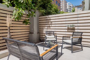 An outdoor seating area with two chairs and a table, a wooden fence, and a tree. - Large Terrace Studio · Selected Design (H02) (Providencia)