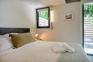 A bedroom with a bed, pillows, a bedside lamp, a window with a view of greenery, and a framed picture on the wall. - Large Terrace Studio · Selected Design (H02) (Providencia)