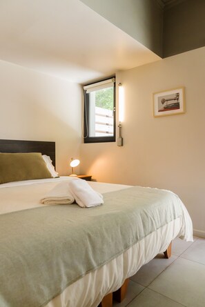 A neatly made bed with a white comforter and a green pillow, a bedside lamp, and a framed picture on the wall. - Large Terrace Studio · Selected Design (H02) (Providencia)