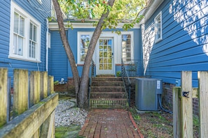 A residential property with a blue exterior, a front door, a small porch, a brick pathway, and a wooden fence. - The Dapper Duck-Downtown Southern Pines! (Southern Pines)