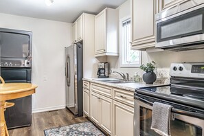 A modern kitchen with stainless steel appliances, a wooden dining table, and a patterned rug. - The Dapper Duck-Downtown Southern Pines! (Southern Pines)