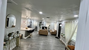 A spacious living area with a sofa, a dining table, and a TV. There are potted plants and a mirror on the walls. - 5-Bedroom Hollywood Home with AC, Room or Entire House (Hollywood)
