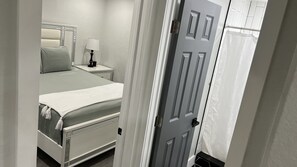 Een slaapkamer met een bed, nachtkastje, lamp en een deur met gordijn.