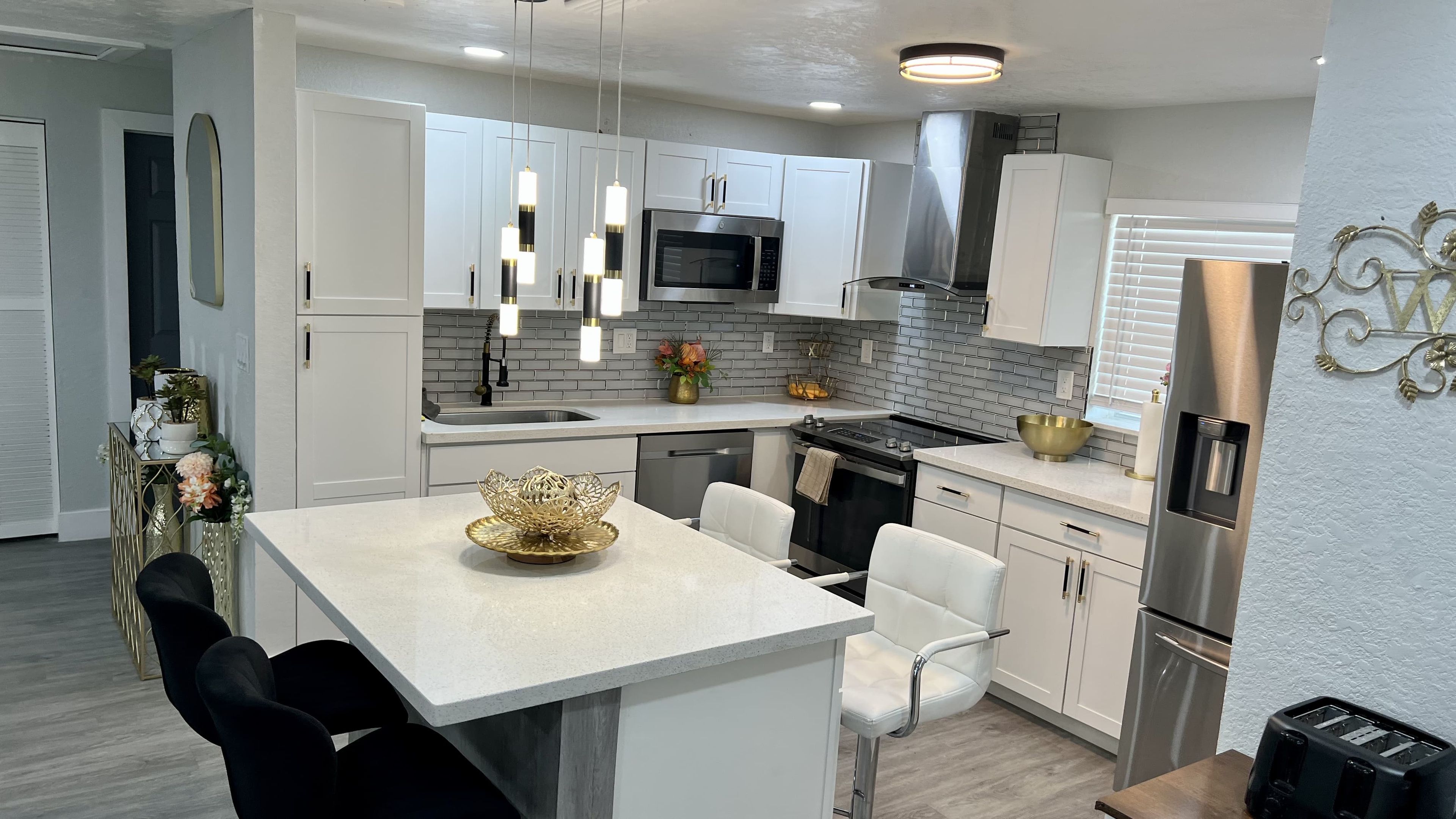 A modern kitchen with white cabinetry, a stainless steel microwave, and a dining area with a white table and chairs.