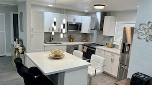 A modern kitchen with white cabinetry, a stainless steel microwave, and a dining area with a white table and chairs. - 5-Bedroom Hollywood Home with AC, Room or Entire House (Hollywood)