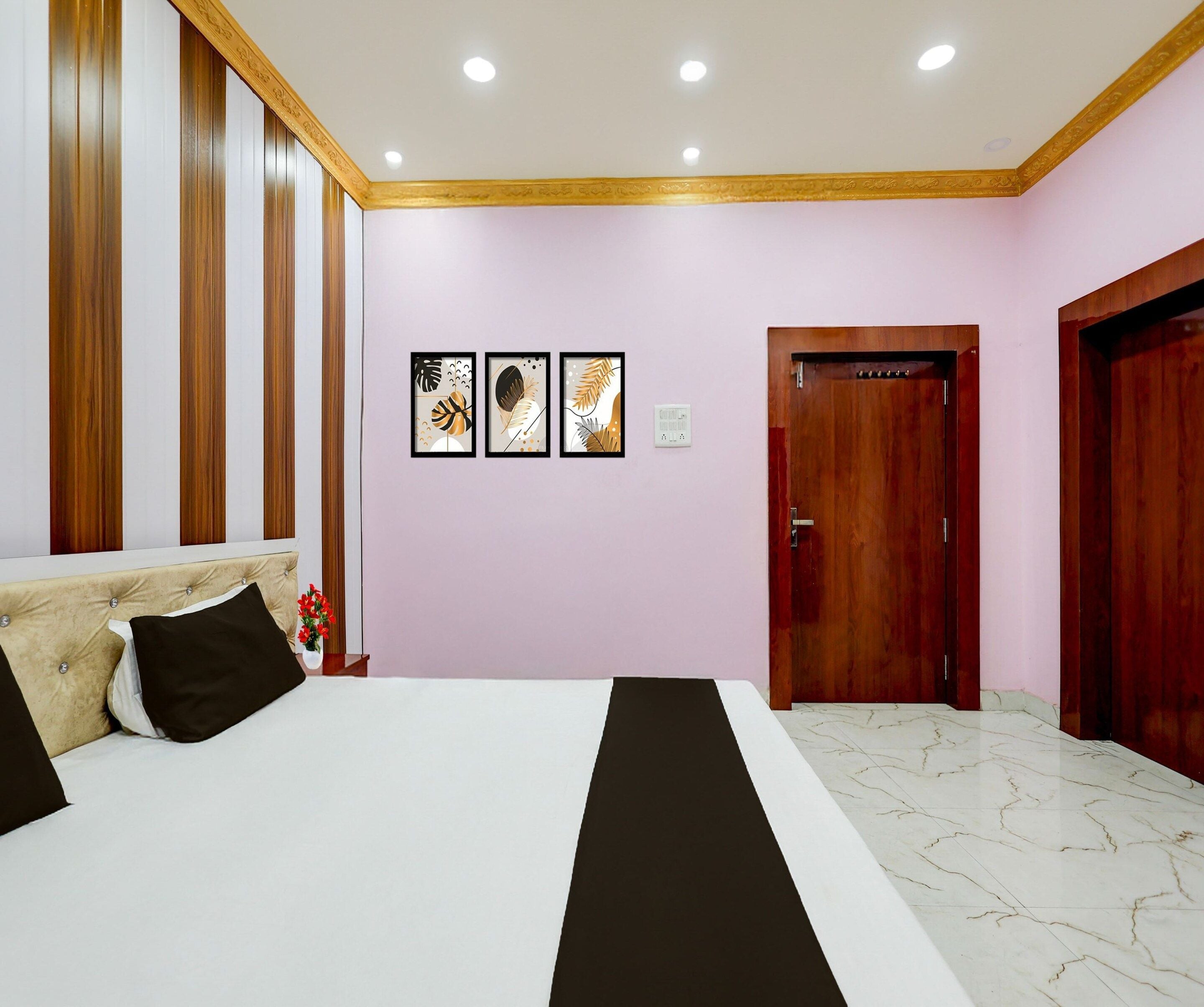 A hotel room with a bed, a wooden wardrobe, a door, and three framed artworks on the wall.