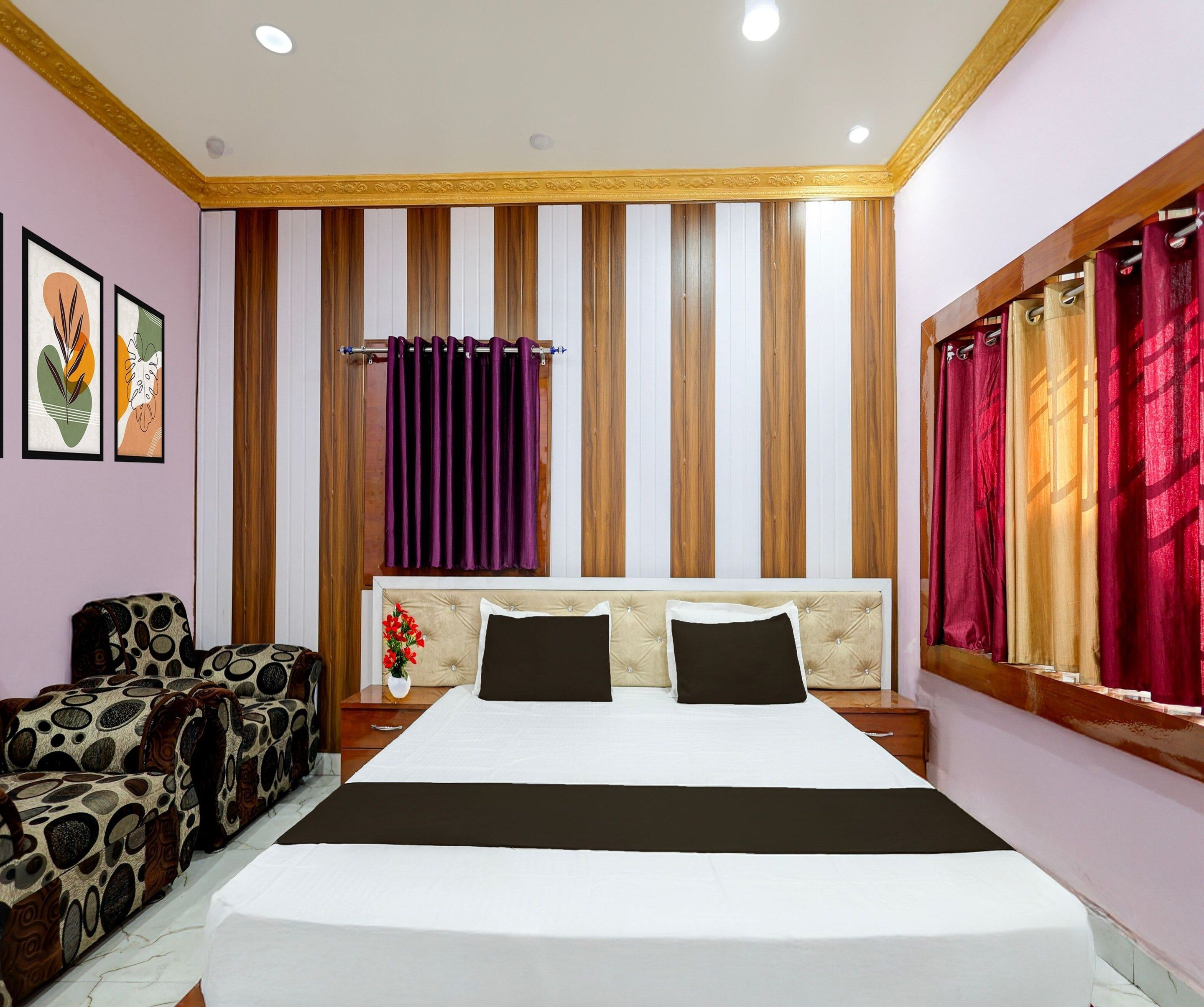 A hotel room with a large bed, a wooden headboard, a nightstand with a vase of flowers, and a sofa with a patterned upholstery.