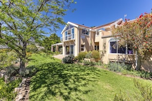A two-story house with a well-maintained lawn, a patio, and a variety of plants and shrubs. - Pure Nature: The Somerset West Wine Region. Ideal for mountain bikers, hikers, and nature lovers (Sir Lowry's Pass)