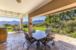 A covered patio with a table and chairs, a wooden barrel, and a view of mountains. - Pure Nature: The Somerset West Wine Region. Ideal for mountain bikers, hikers, and nature lovers (Sir Lowry's Pass)