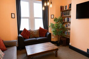 A living room with a sofa, a coffee table, a bookshelf, and a television. - Cardiff | 4BR | Sleeps 10 | Groups | Contractors (Cardiff)