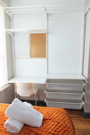 Quarto de hotel com cama, escrivaninha e caixas organizadoras.