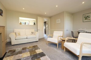 A living room with a sofa, chairs, a rug, and a dining area with a table and chairs. - Ross-on-Wye Cottage | River Fishing | 2 Baths (Bridstow)