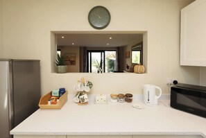A kitchen with a central island, a clock above it, and a view into the living area through a window. - Ross-on-Wye Cottage | River Fishing | 2 Baths (Bridstow)