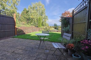A patio with a table and chairs, surrounded by a wooden fence and a garden. - Ross-on-Wye Cottage | River Fishing | 2 Baths (Bridstow)