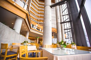 Ein mehrgeschossiges Interieur mit einem zentralen Atrium, ausgestattet mit einem Glastisch und -stühlen, und Blick auf die oberen Stockwerke.