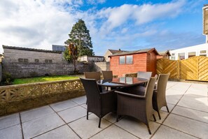 An outdoor patio with a table and chairs, a wooden fence, and a brick wall. - 4-Bed House Sleeps 8 · Free Parking & Patio · 1 Min to Margam Deer Pub (Neath Port Talbot)