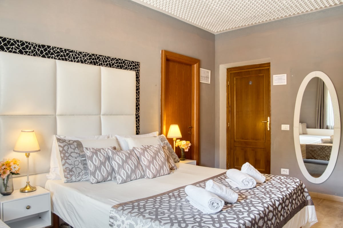 A hotel room with a large bed, a bedside table with a lamp, a mirror, and a door.