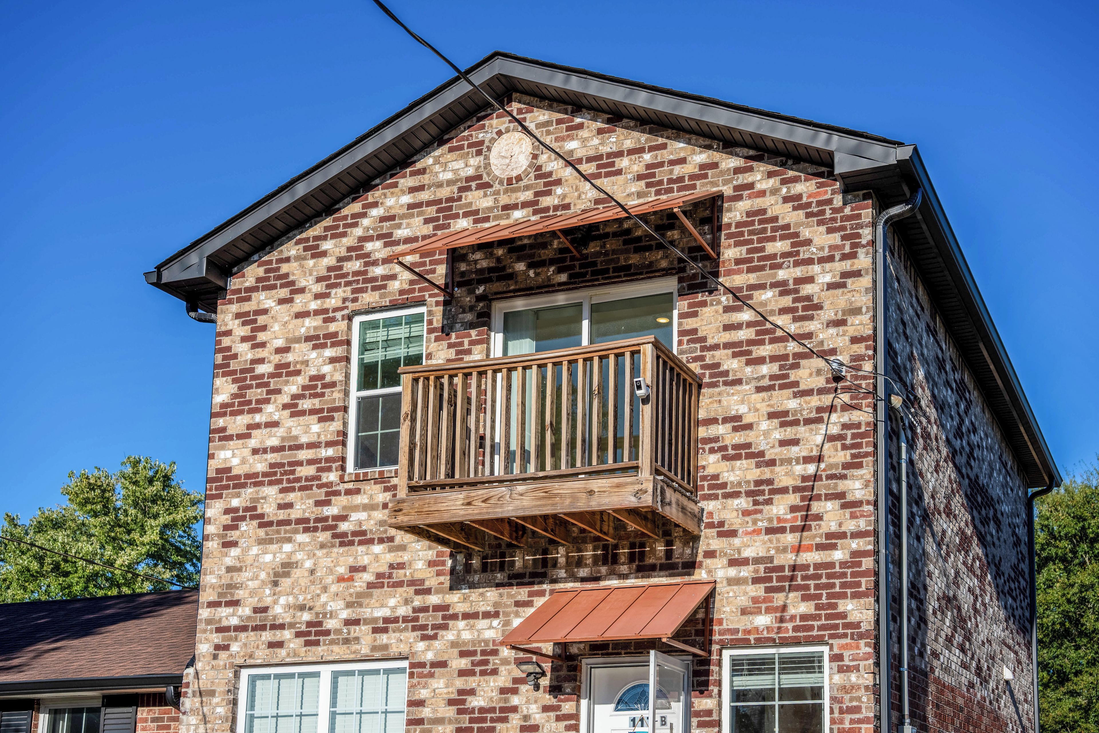 A two-story brick building with a wooden balcony, a small porch, and a garage door.