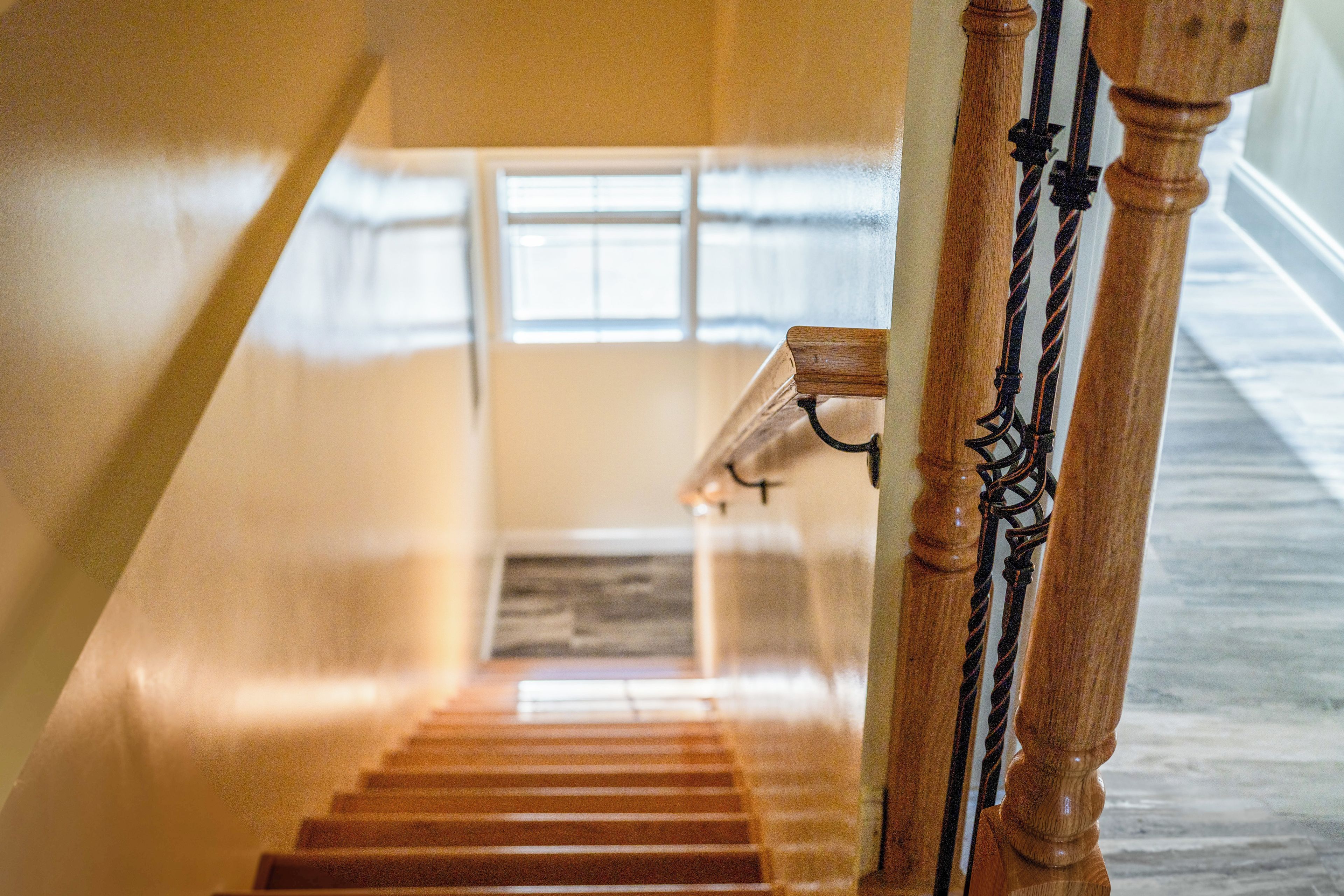 Una escalera de madera con barandilla y un ventanal en la parte superior.