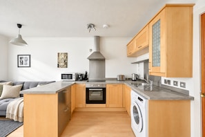 A compact kitchen with wooden cabinets, a built-in oven, a washing machine, and a coffee maker. - Charming Edinburgh Flat near Royal Mile (Edinburgh)