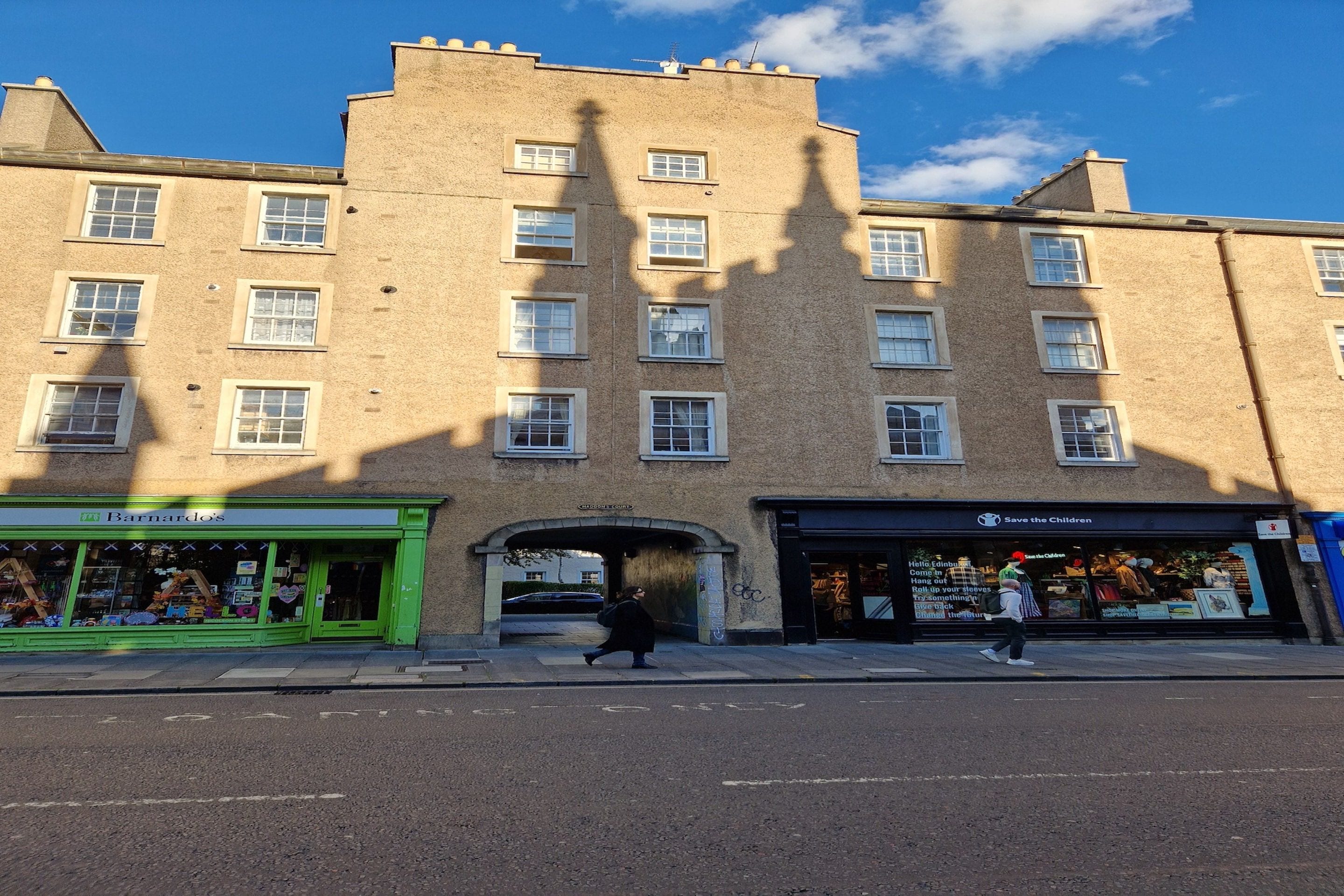 A multi-story building with a central archway, storefronts on either side, and a clear sky.