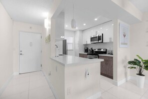 A modern kitchen with white cabinetry, a central island, and a microwave. - Le Cartier 406 STR-03610 (Sunny Isles Beach)